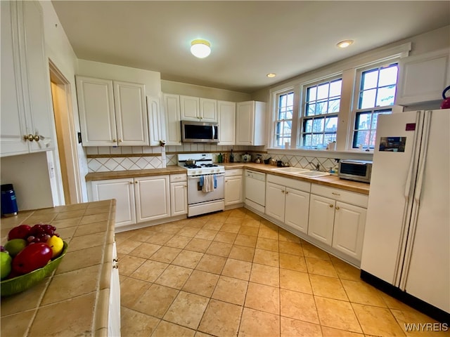 kitchen with tile countertops, white appliances, white cabinets, sink, and decorative backsplash