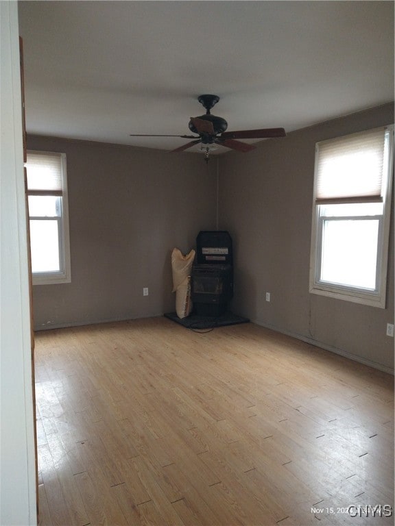 spare room with ceiling fan, light wood-type flooring, a wood stove, and a wealth of natural light