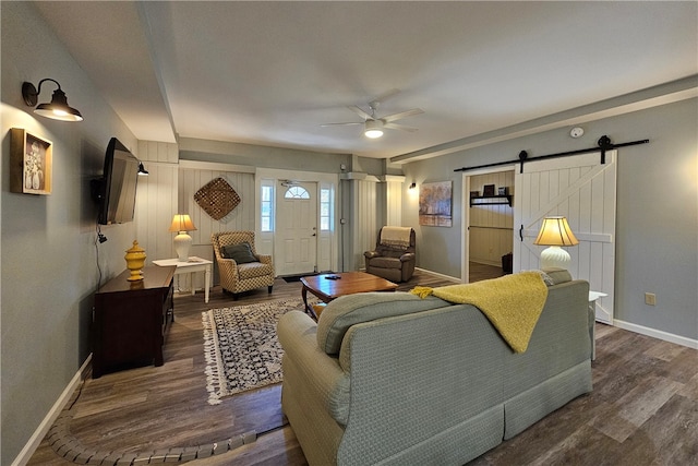 living room with ceiling fan, a barn door, and dark hardwood / wood-style flooring