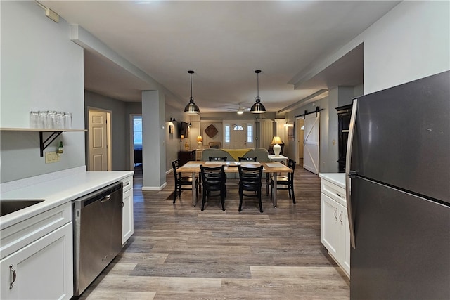 kitchen with pendant lighting, white cabinets, a barn door, light hardwood / wood-style floors, and stainless steel appliances