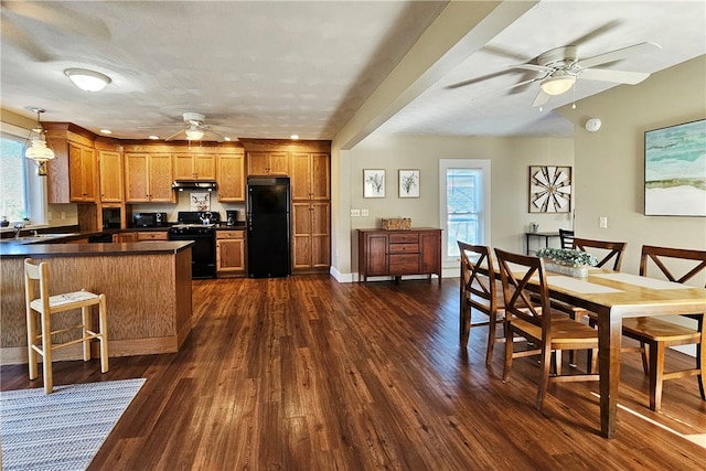 kitchen featuring a kitchen bar, dark hardwood / wood-style flooring, sink, black appliances, and pendant lighting