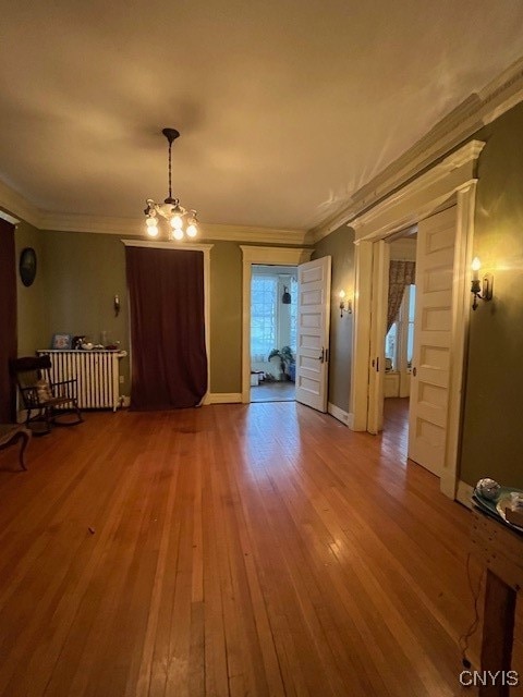 unfurnished living room featuring radiator heating unit, hardwood / wood-style floors, a chandelier, and ornamental molding