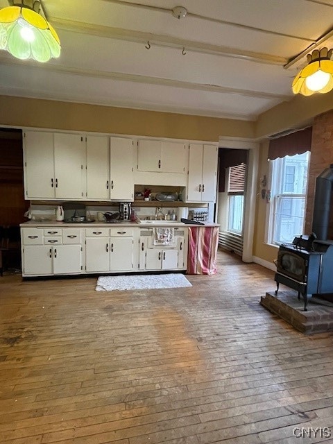 kitchen featuring a wood stove, sink, light hardwood / wood-style flooring, beamed ceiling, and white cabinets