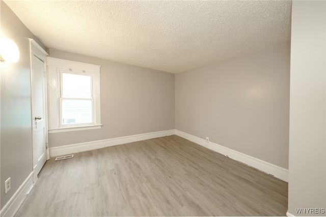 empty room with a textured ceiling and light hardwood / wood-style floors