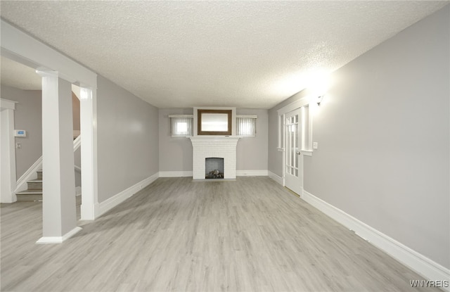 unfurnished living room featuring light hardwood / wood-style floors, a textured ceiling, and a brick fireplace