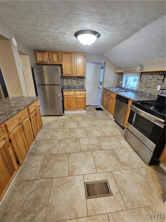 802 W End Ave, Wilna, NY 13619 - kitchen with appliances with stainless steel finishes, backsplash, vaulted ceiling, a sink, and brown cabinetry