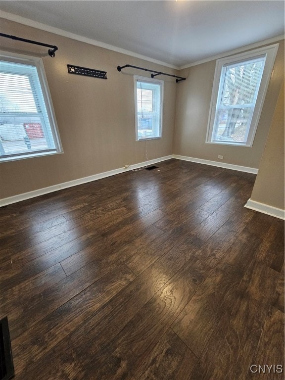 empty room featuring a healthy amount of sunlight, ornamental molding, and dark wood-type flooring