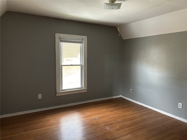 spare room with hardwood / wood-style floors and vaulted ceiling