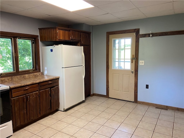 kitchen with dark brown cabinetry, a paneled ceiling, light tile patterned floors, and white appliances