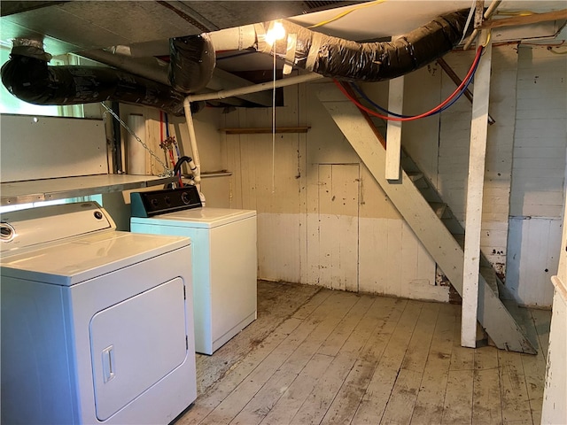 laundry area with light hardwood / wood-style floors, separate washer and dryer, and wooden walls