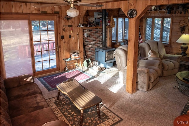 carpeted living room with a wood stove, wooden walls, and ceiling fan