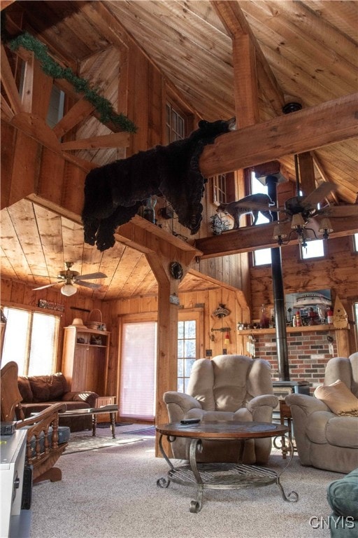 carpeted living room featuring beam ceiling, ceiling fan, high vaulted ceiling, wood walls, and wood ceiling