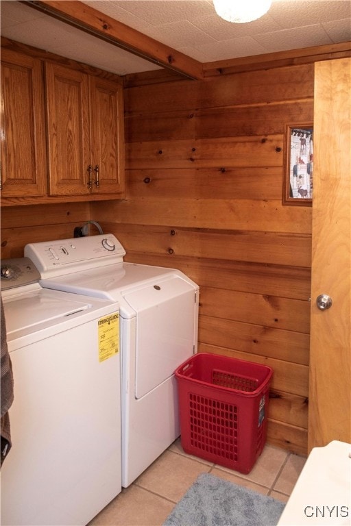 laundry room featuring separate washer and dryer, wooden walls, light tile patterned floors, and cabinets