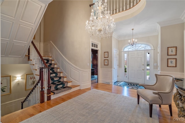 entrance foyer with a notable chandelier, a towering ceiling, crown molding, and light hardwood / wood-style flooring