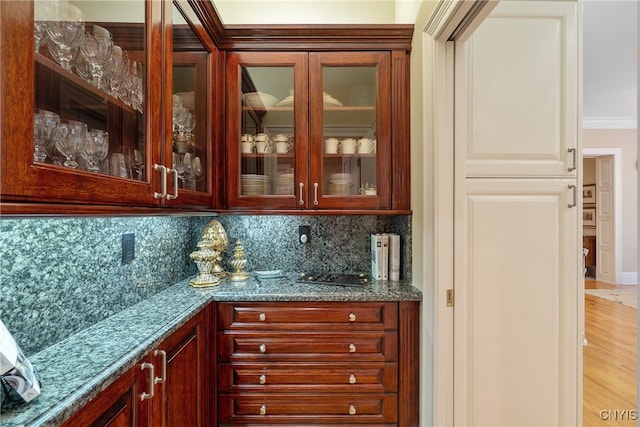 bar with dark stone counters, light hardwood / wood-style floors, tasteful backsplash, and ornamental molding