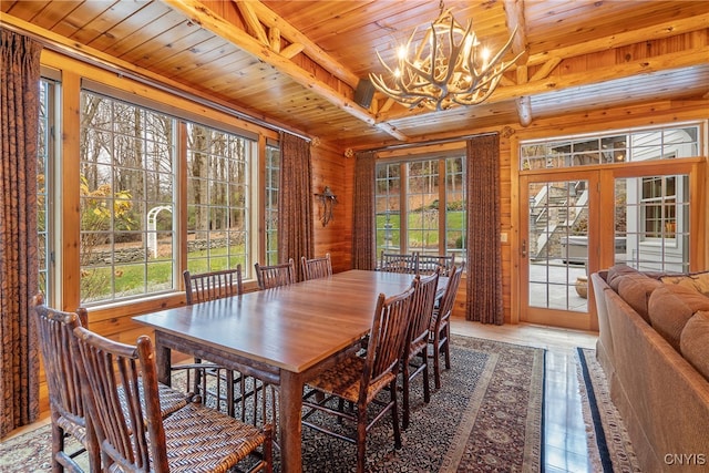 dining space featuring french doors, wooden walls, a notable chandelier, beam ceiling, and wood ceiling