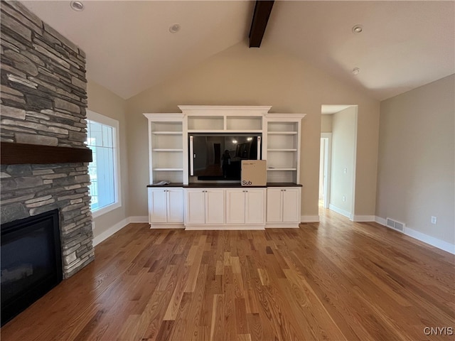 unfurnished living room with beam ceiling, a fireplace, high vaulted ceiling, and light wood-type flooring