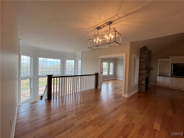 empty room with hardwood / wood-style floors, a stone fireplace, and a chandelier