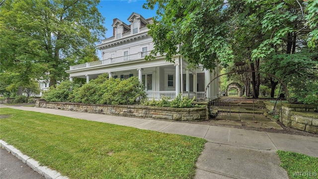 view of front facade with a porch, a balcony, and a front lawn