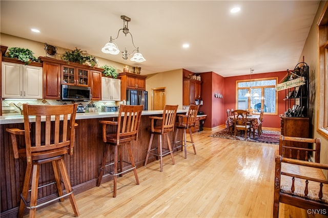 kitchen featuring black refrigerator, hanging light fixtures, light hardwood / wood-style floors, a kitchen bar, and a chandelier