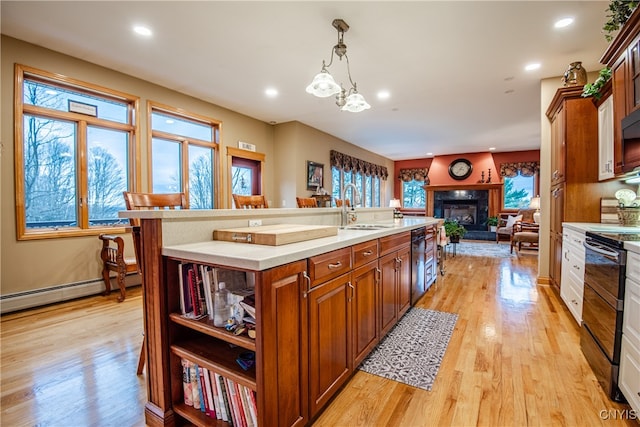 kitchen with light wood-type flooring, black appliances, sink, pendant lighting, and an island with sink