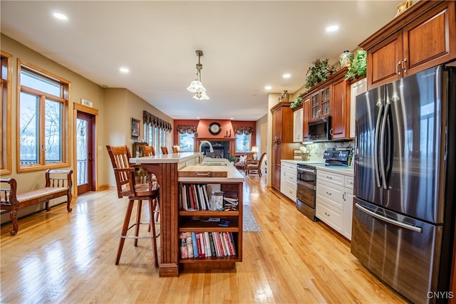 kitchen featuring hanging light fixtures, backsplash, a center island with sink, appliances with stainless steel finishes, and light wood-type flooring