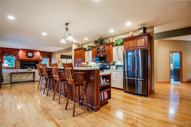 kitchen featuring a kitchen bar, appliances with stainless steel finishes, pendant lighting, light hardwood / wood-style flooring, and a center island