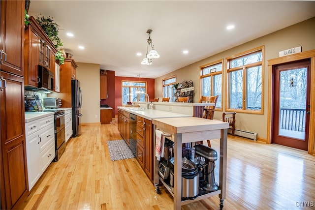 kitchen with sink, baseboard heating, decorative light fixtures, appliances with stainless steel finishes, and light wood-type flooring