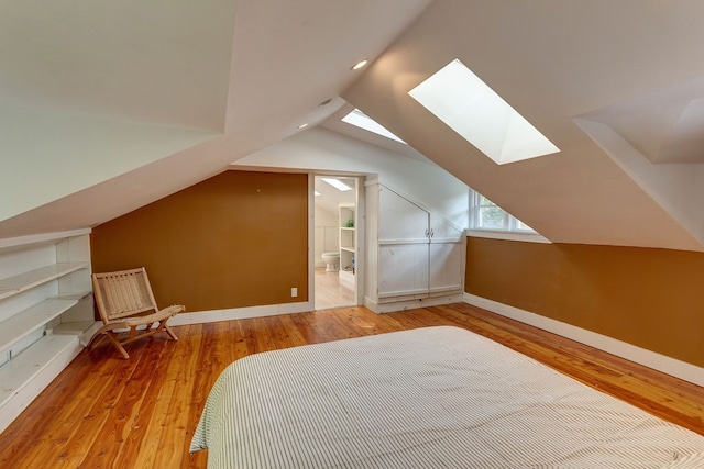 unfurnished bedroom with connected bathroom, vaulted ceiling with skylight, and light wood-type flooring