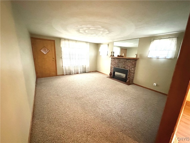 unfurnished living room with carpet floors, a brick fireplace, and a wealth of natural light