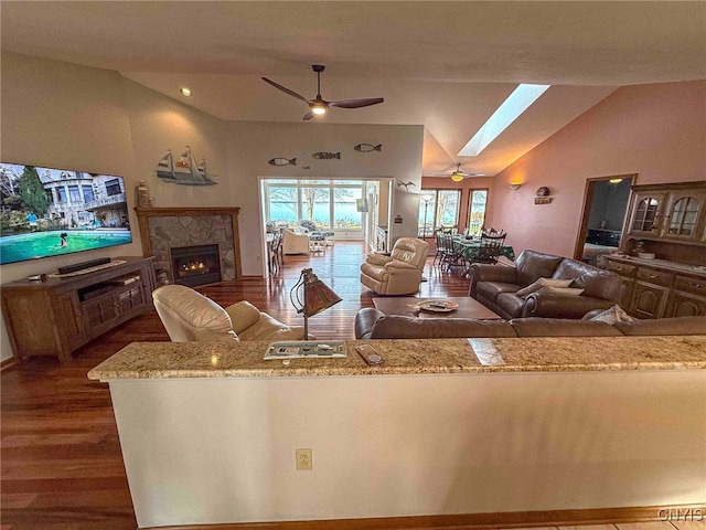 kitchen with dark hardwood / wood-style flooring, light stone counters, lofted ceiling with skylight, ceiling fan, and a fireplace