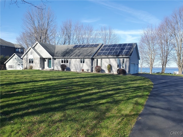 view of front of home with solar panels, a garage, a water view, and a front yard