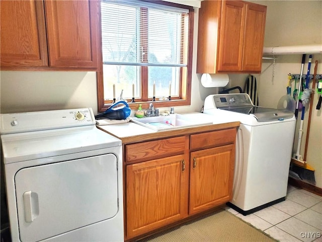 laundry area featuring washing machine and dryer, sink, light tile patterned floors, and cabinets