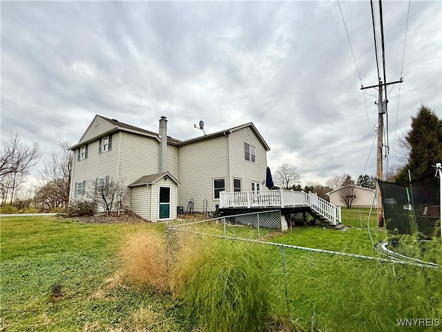 back of property with a lawn, a trampoline, and a wooden deck