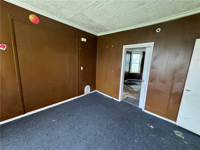 unfurnished bedroom featuring wooden walls, ornamental molding, a textured ceiling, and dark colored carpet