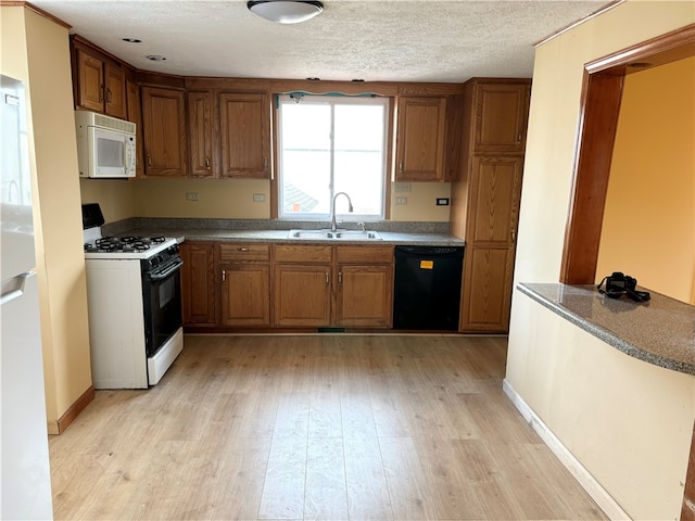 kitchen with a textured ceiling, light wood-type flooring, white appliances, and sink