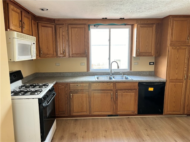 kitchen with a textured ceiling, white appliances, sink, and light hardwood / wood-style flooring