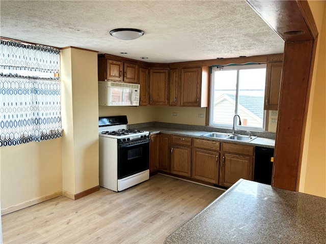 kitchen with a textured ceiling, light wood-type flooring, white appliances, and sink