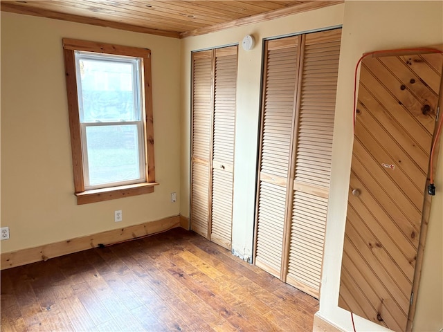 unfurnished bedroom featuring multiple closets, crown molding, wooden ceiling, and light wood-type flooring