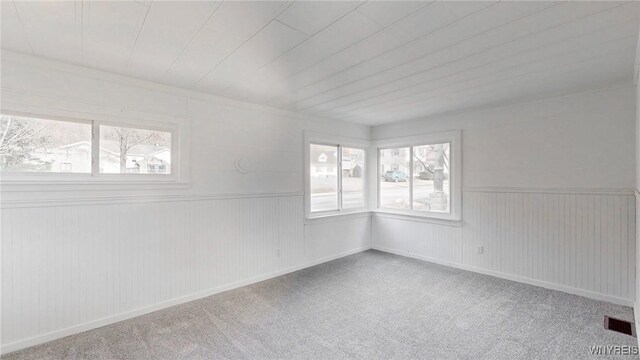 empty room featuring carpet flooring, a healthy amount of sunlight, visible vents, and a wainscoted wall