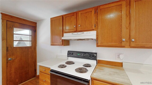 kitchen with light countertops, brown cabinets, under cabinet range hood, and range with electric stovetop