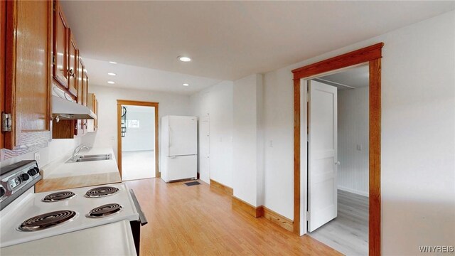 kitchen featuring under cabinet range hood, light countertops, light wood-style flooring, white appliances, and a sink