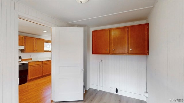 kitchen featuring under cabinet range hood, light countertops, light wood-type flooring, brown cabinets, and range with electric stovetop