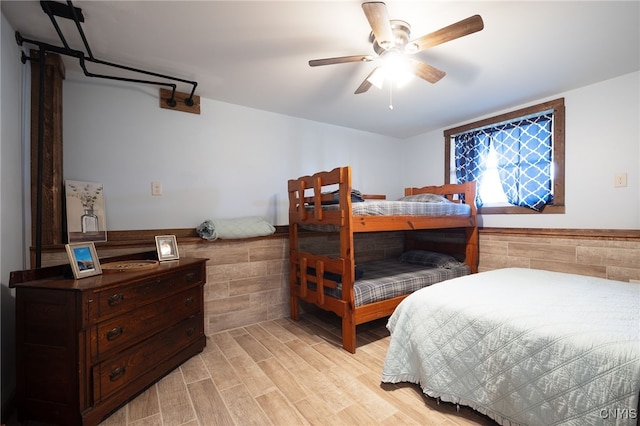 bedroom with light hardwood / wood-style flooring, ceiling fan, and tile walls