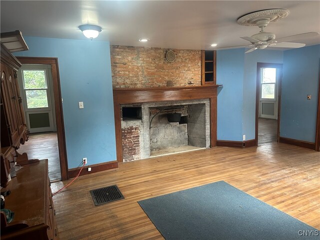 unfurnished living room featuring a healthy amount of sunlight, a fireplace, ceiling fan, and wood-type flooring