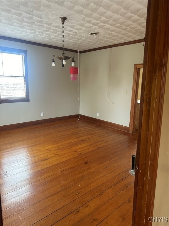 empty room featuring a notable chandelier, wood-type flooring, and crown molding