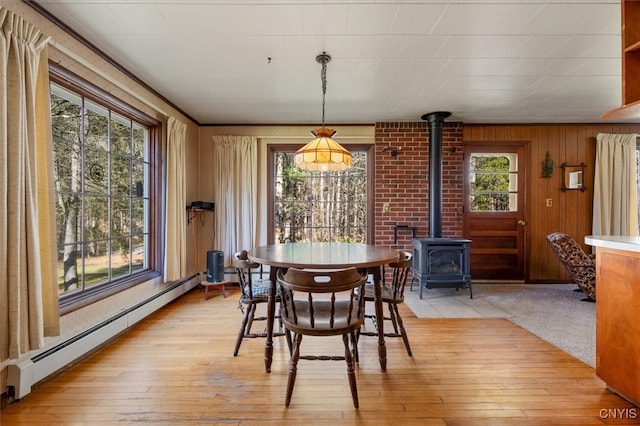 dining room with a baseboard radiator, a wood stove, light hardwood / wood-style floors, and wood walls