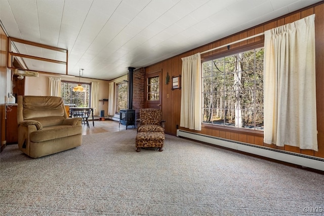 living room featuring baseboard heating, a wood stove, a wealth of natural light, and wood walls