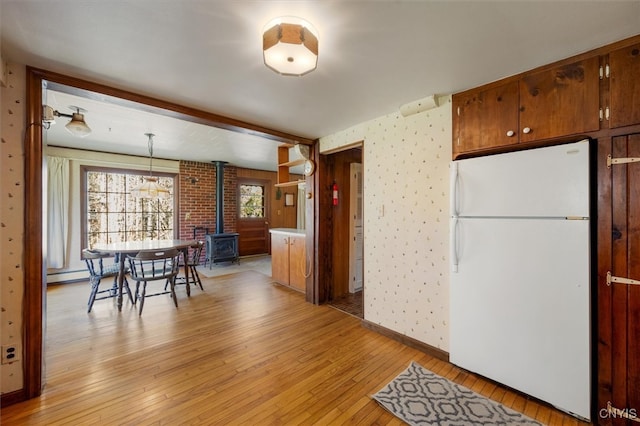 kitchen featuring light wood-type flooring, a baseboard heating unit, decorative light fixtures, white fridge, and a wood stove