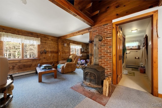 living room featuring carpet flooring, a wood stove, baseboard heating, and wood walls